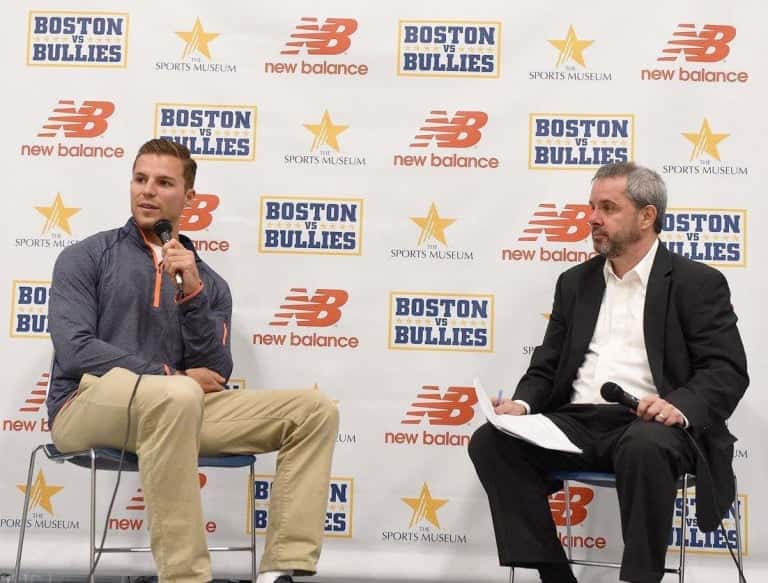 Justin Turri holding a microphone, seated next to another man in front of a promotional wall